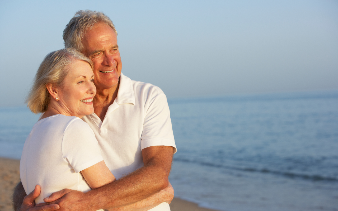 Elder man and woman smiling and standing next to the sea