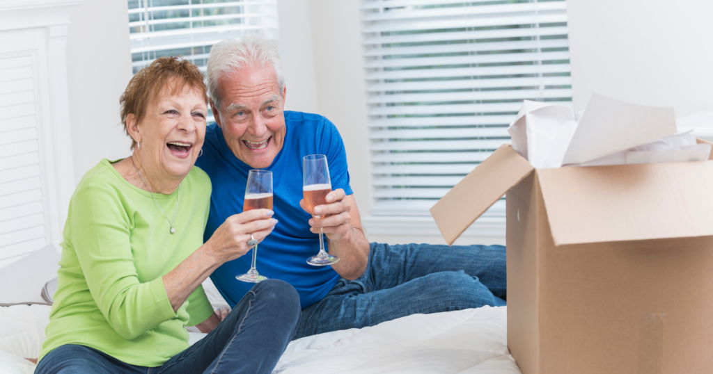 Senior Couple drinking pink champagne with box of papers in front of them Senior Couple drinking pink champagne with box of papers in front of them